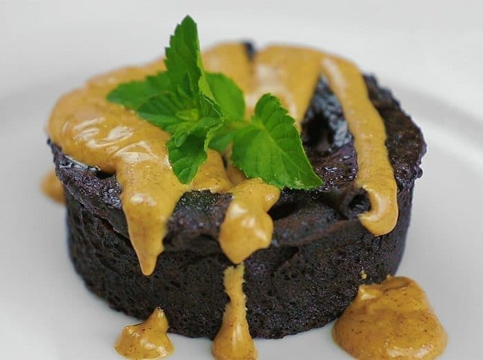 A chocolate muffin with brown dessert sauce and a green garnish sitting on a white surface