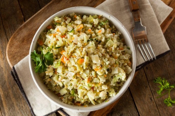 A bowl of Roasted Broccoli with Cauliflower “Rice” and Sauteed Onions sitting on a wooden table