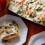 Two plates of root vegetable lasagna next to a full dish sitting on a wooden table
