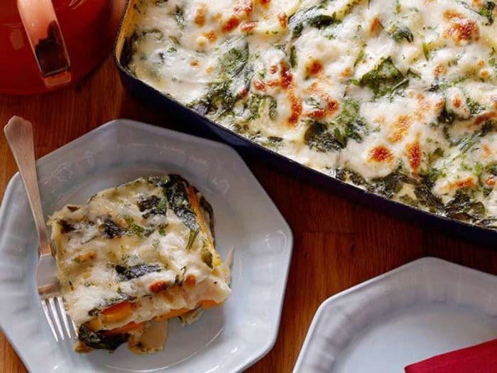 Two plates of root vegetable lasagna next to a full dish sitting on a wooden table