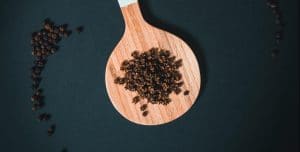 Black pepper fruit extract Black pepper in a wooden spoon on a dark table