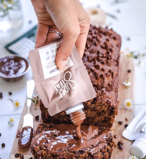Woman pouring a packet of SuperFat Keto Nut Butter on a loaf of chocolate bread.