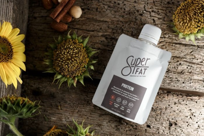 A packet of SuperFat protein flavor on a wooden table with sunflowers surrounding it.
