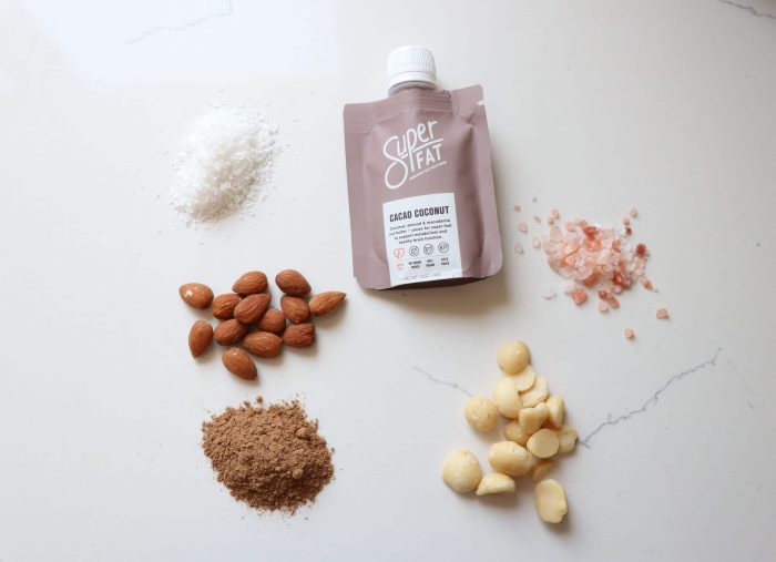 A bottle of SuperFat cacao coconut laying on a white counter top with its ingredients around it.