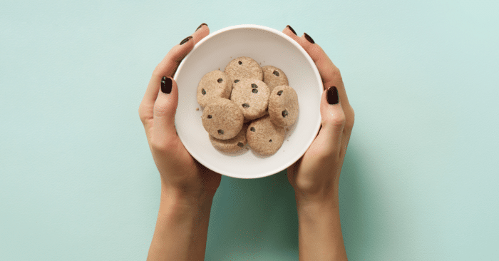 Woman's hands holding a bowl of SuperFat chocolate chip cookie bites on a green background