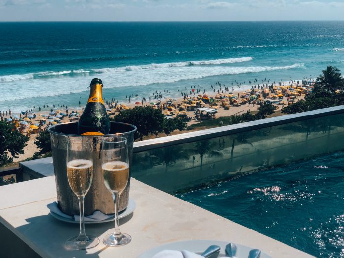 Two glasses of champagne and a bottle of champagne sitting on a ledge overlooking the ocean.