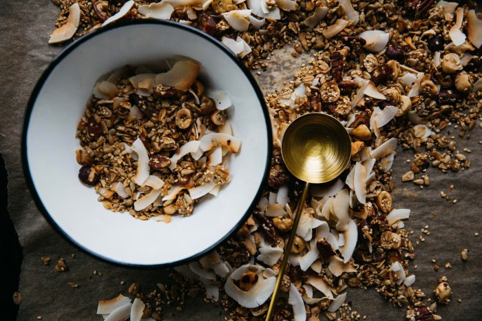 A white bowl is full of oats sitting on a brown surface with a copper spoon next to it.