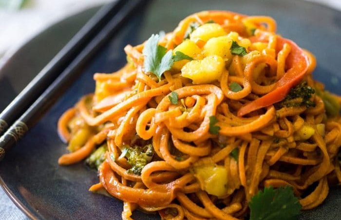 A black plate of sweet potato coconut curry noodles with black chopsticks sitting next to it