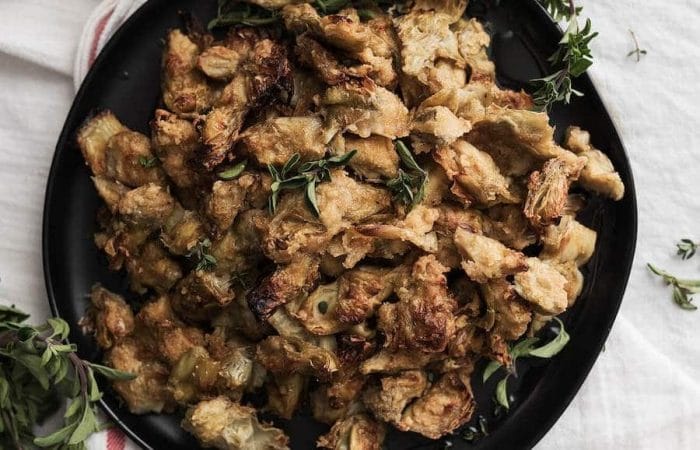 A bowl of baked and fried artichoke hearts sitting on a white marble surface